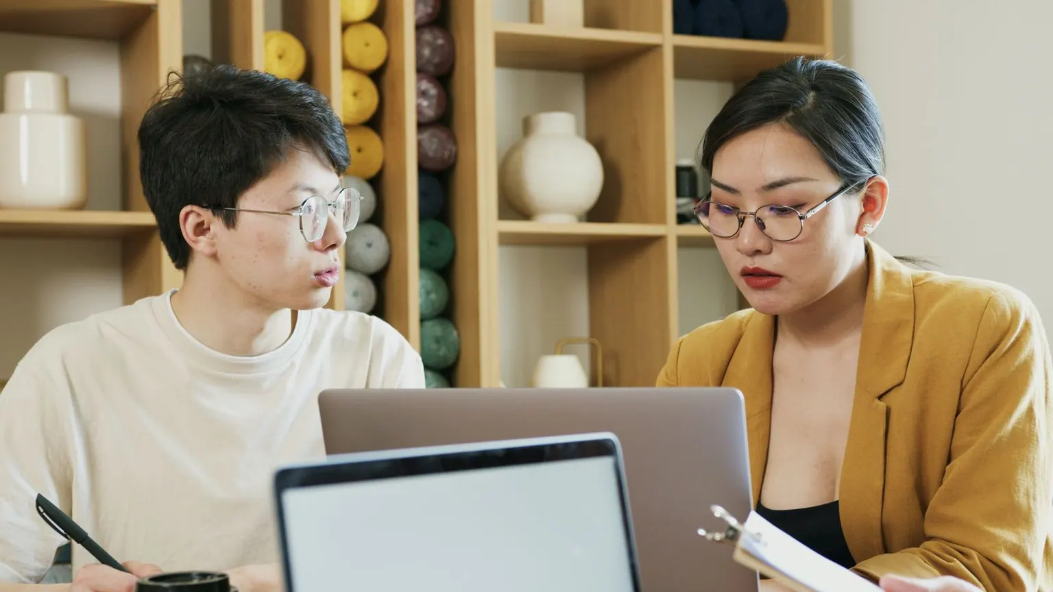 Two Asian finance professionals reviewing numbers together on laptops.