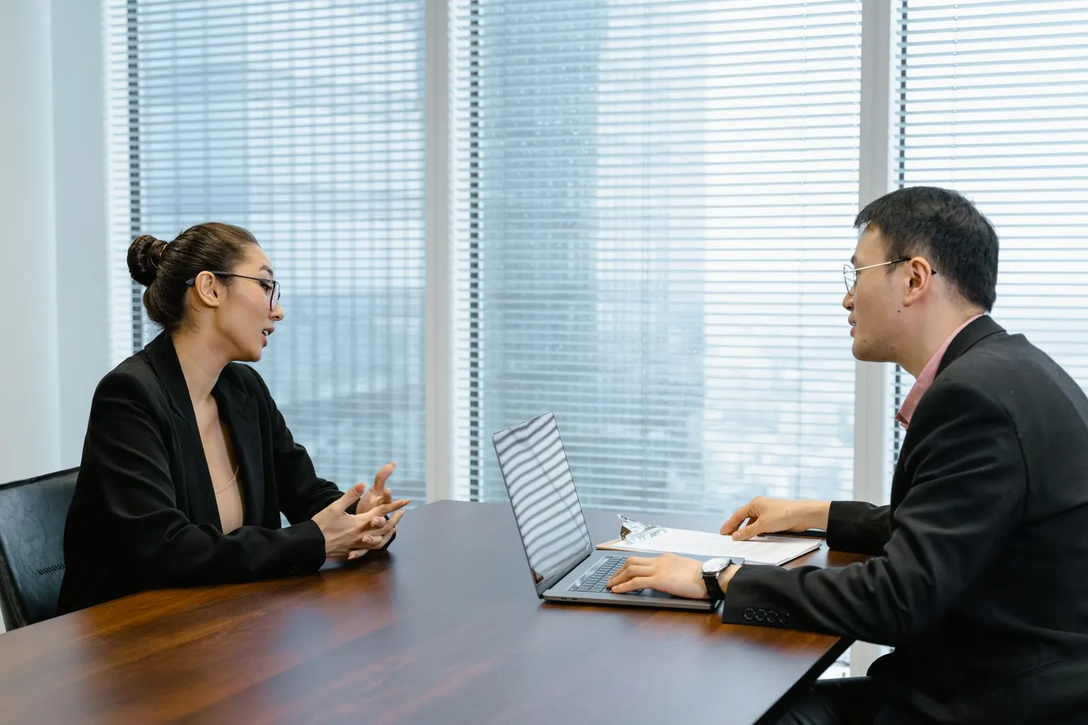 Two Asian professionals in an interview conversation at an office table.