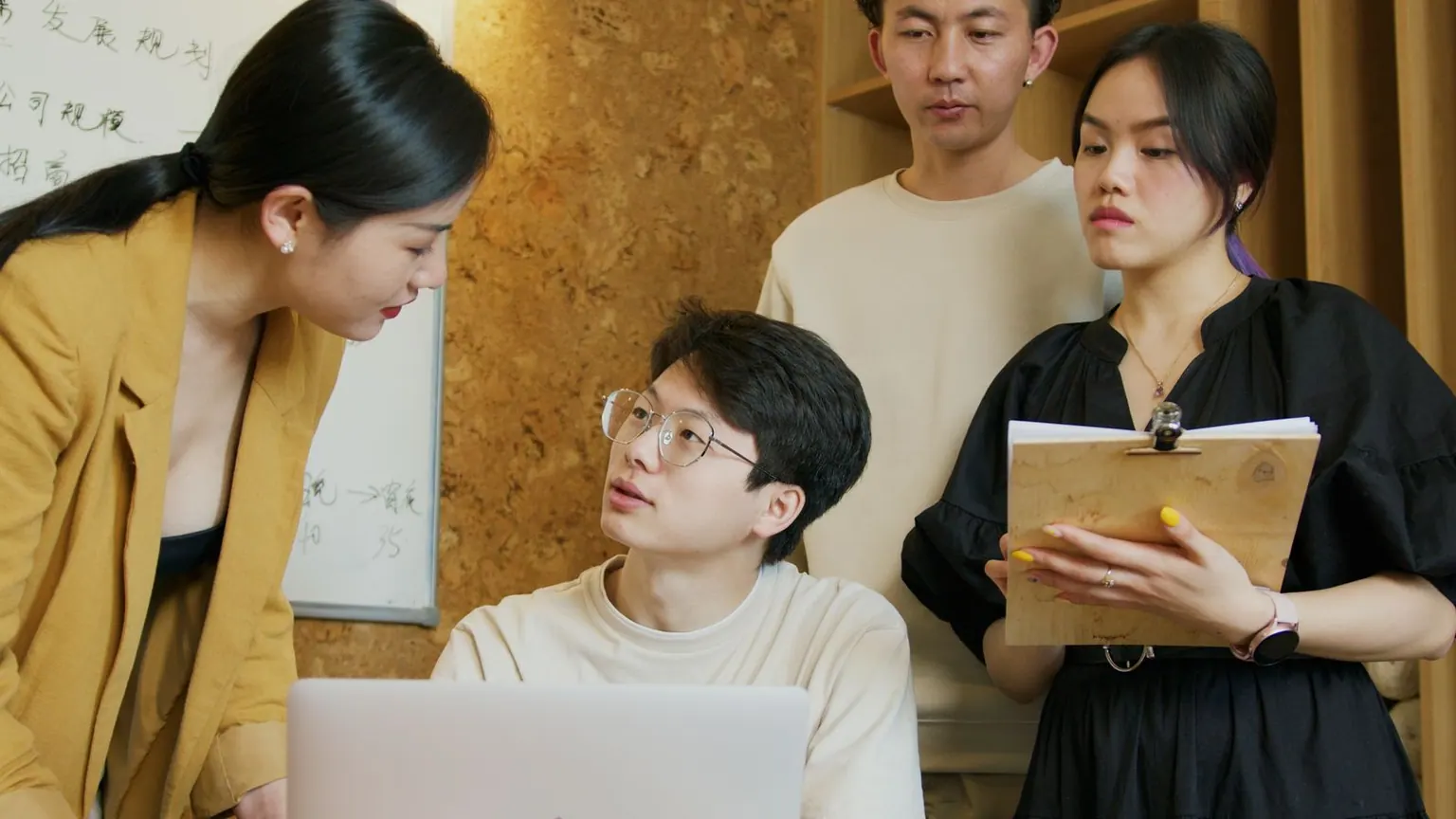 An Asian team coaching session around a laptop in a warm office space.
