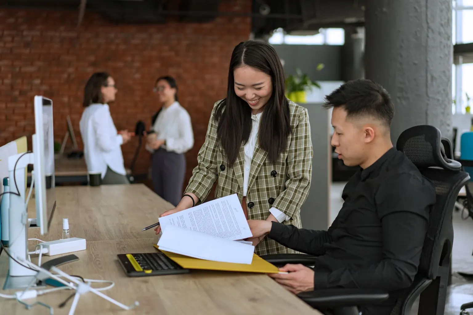 Asian colleagues reviewing handover documents together at an office desk.