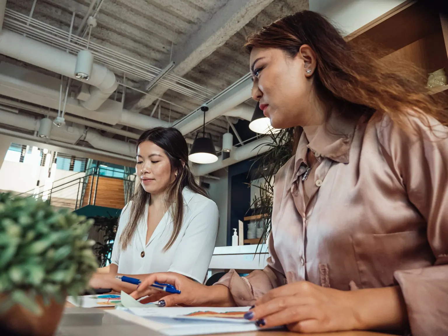 Two Asian colleagues working together at desks in an open-plan office.