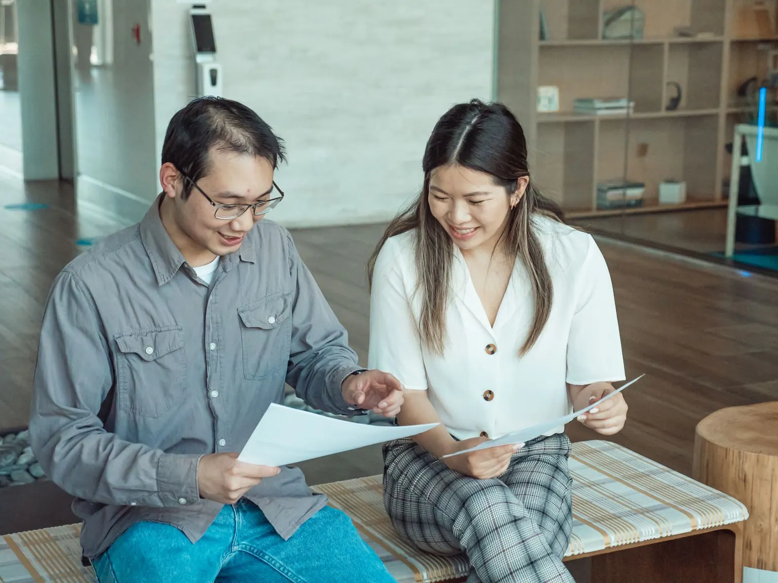 Two colleagues having a discussion while reviewing documents in a modern office setting.