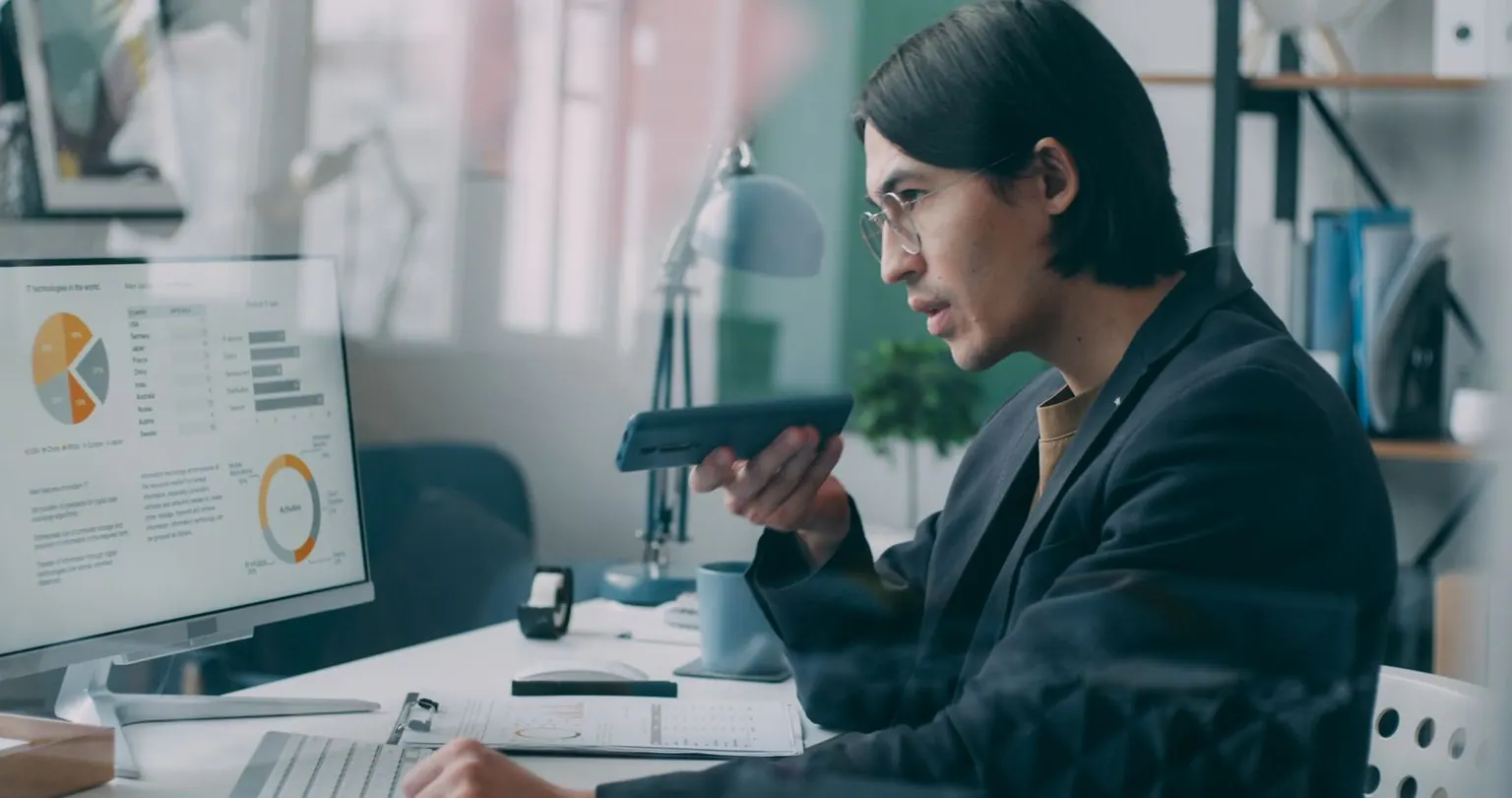 An Asian engineer reviewing dashboards on screen while taking a call in an office.