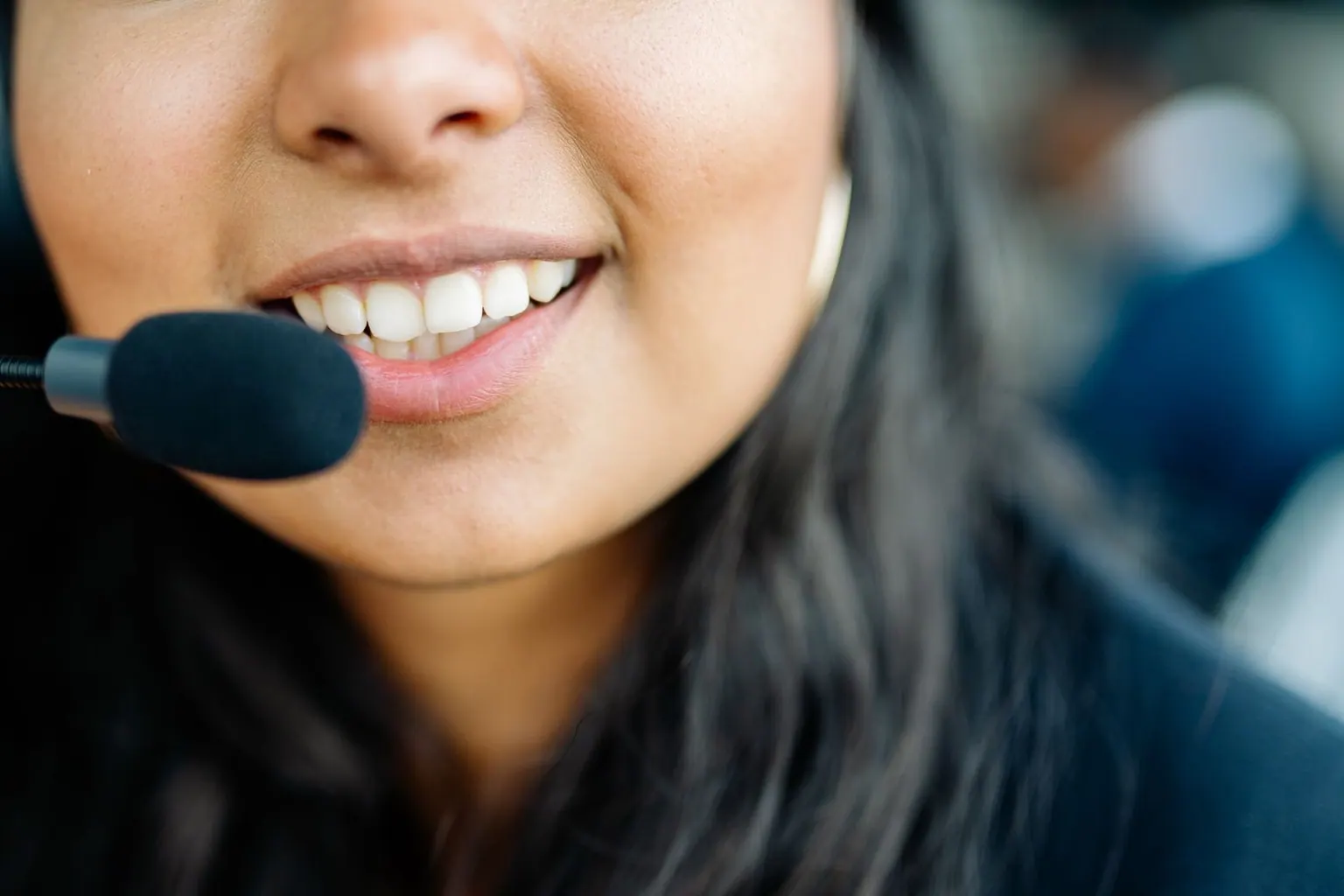 Close-up of an Asian agent speaking into a headset microphone during a customer call.