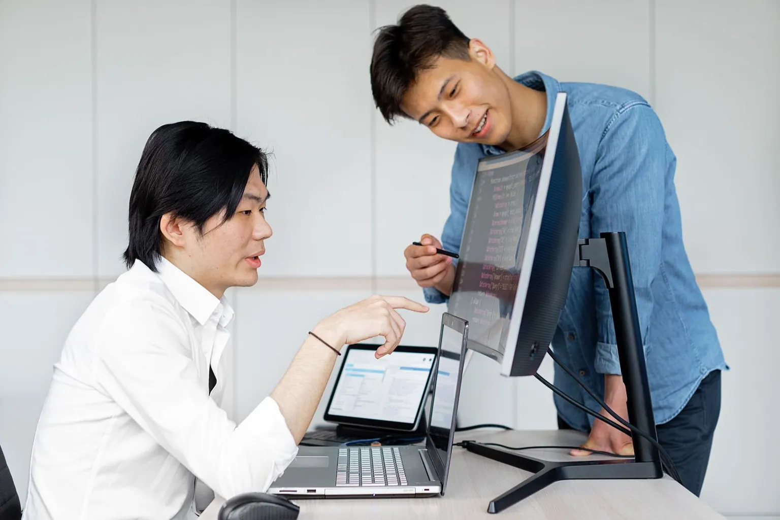 Two Asian engineers standing at a monitor together during a quick working session.