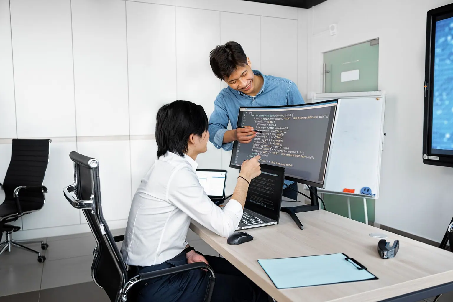 An Asian engineer walking a new team member through their setup on a monitor.