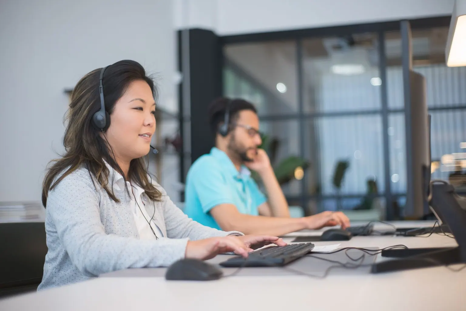Support agents wearing headsets working side by side at computers in an office.
