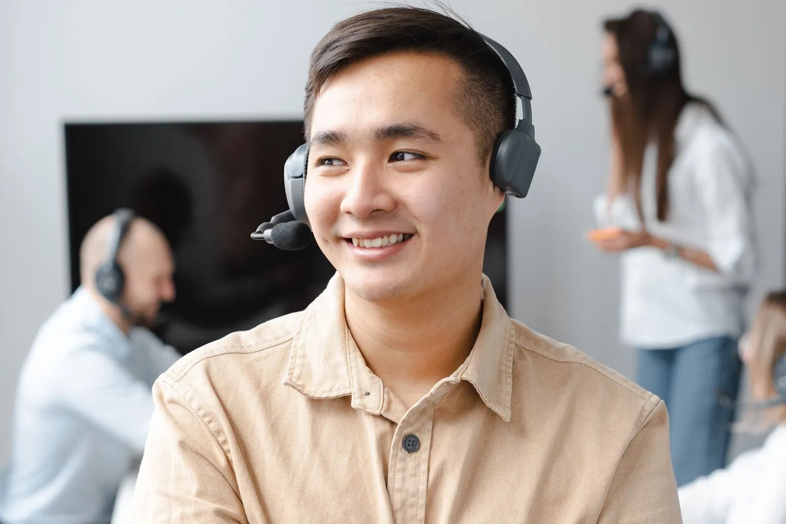 A smiling Asian sales representative wearing a headset in a modern office.