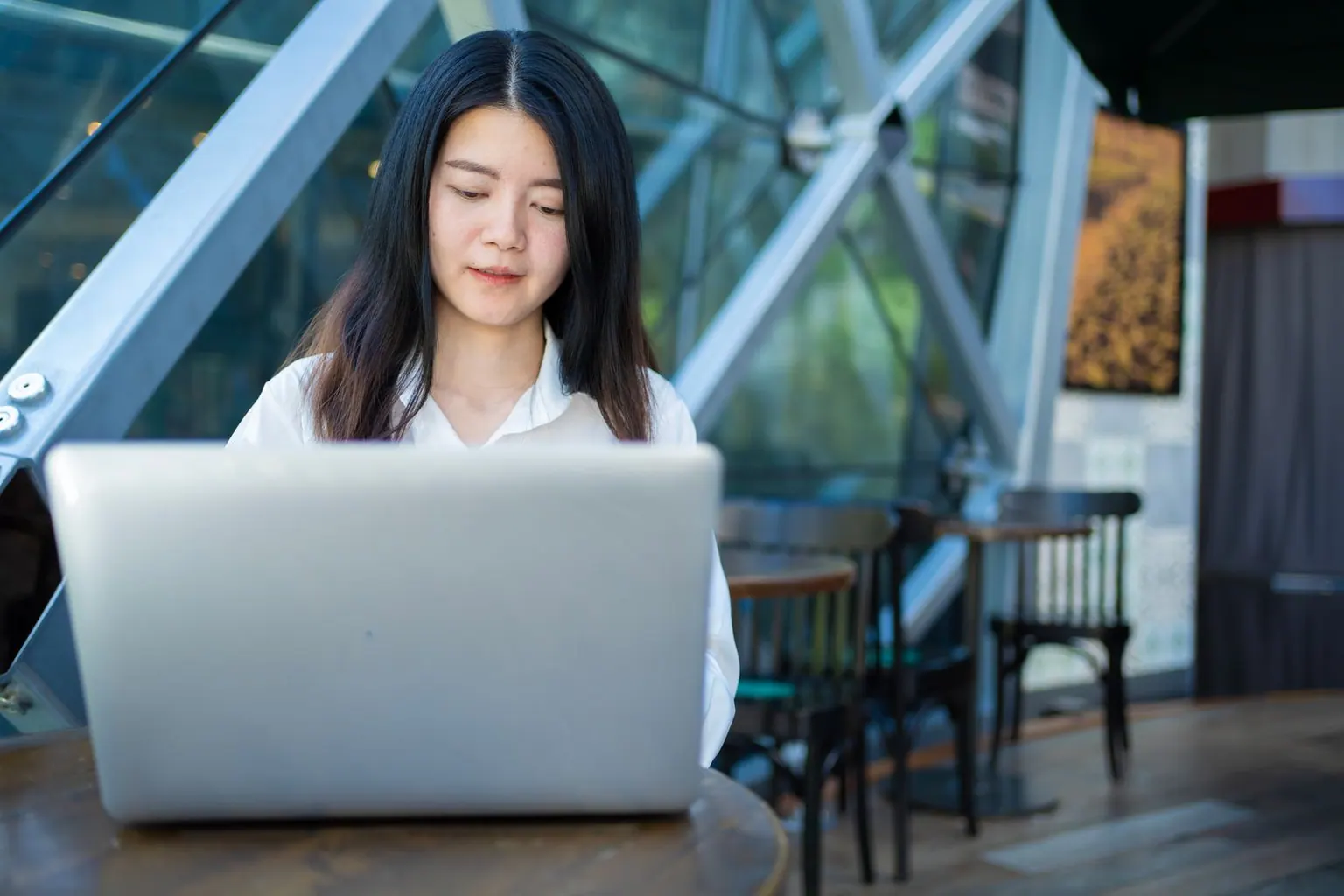 An Asian freelancer working on a laptop in a bright cafe.